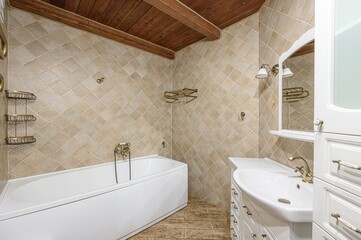 cozy bathroom features a white bathtub and sink, accented with beige diamond-patterned tiles, brass fixtures, and a rustic wooden ceiling