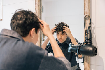 Teenager girl styling hair in bathroom mirror during morning routine
