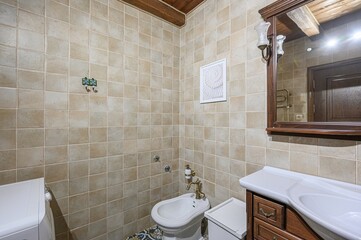 rustic bathroom with beige tile walls, a wooden ceiling beam, a bidet, a wooden vanity, and a framed shell print