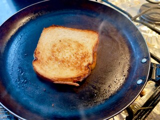 Uma fatia de pão perfeitamente tostada, dourada e estaladiça, numa frigideira quente com vapor visível. Conceito de pequeno-almoço simples, comida caseira e o dia a dia na cozinha.