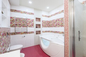bright bathroom featuring floral tile accents, white fixtures like a jacuzzi tub and toilet, pink...