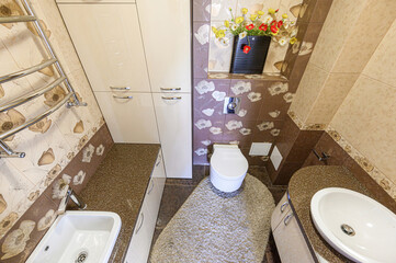 Cozy bathroom featuring floral-patterned tiles, white cabinets, a bidet, toilet, and a soft rug. A...