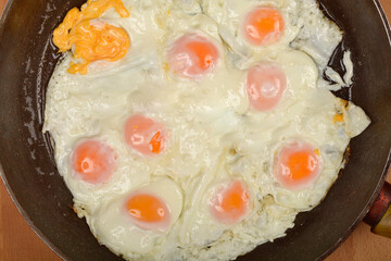 A top-down view of multiple fried eggs cooking in a pan on a wooden surface