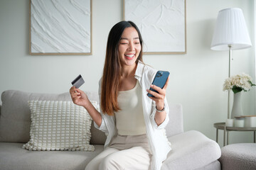 Cheerful woman managing finances, shopping online or paying bills with credit card and phone.