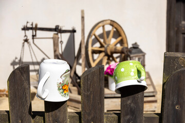 Traditional enamel mugs on rural wooden fence with vintage wagon wheel