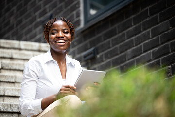 Portrait of beautiful African woman in elegant suit holding tablet computer in business district.