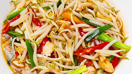 Stir-fried bean sprouts with salted fish, red chilies, and spring onions served on a white plate – a traditional Asian dish, presented in a close-up.