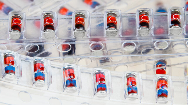 Closeup of SMD Zener diodes packaged in clear plastic blister pack strips on a white background. Pile of red electronic components in transparent packaging. Semiconductor surface mount devices on PCB.