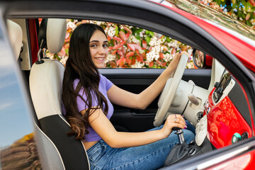 Young woman driving a red car, holding the steering wheel and the gear stick