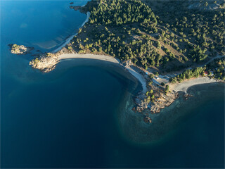 Aerial top view shows the shoreline of a deep blue lake meeting sandy beaches
