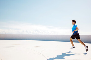 Running Under a Clear Sky at Sunset Atop a Modern Rooftop in an Urban Setting, Showcasing Athletic...