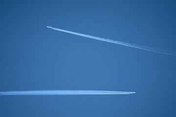 a twin engined jet aircraft and quad engine jet crossing a deep blue sky with contrails at high altitude