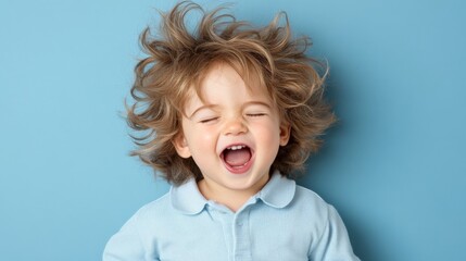 Happy young boy with curly hair laughing against a blue background