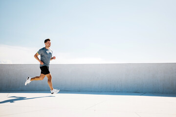Joyful Runner Enjoying a Bright Morning Jog on a Rooftop With a Clear Blue Sky and Distant Clouds...