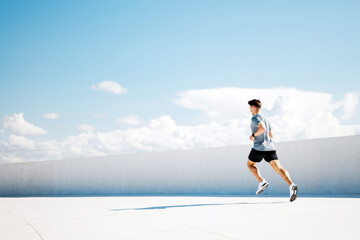 Young Athlete Performing a Dynamic Sprint Under a Clear Blue Sky in an Urban Setting During a Sunny...