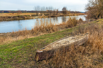 An old wooden rowboat lies on the grass on the bank of a river in the countryside. Siverskyi Donets river in Kharkiv region, Ukraine