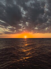 Obraz premium Vibrant red and orange sunset casting warm reflections on gentle ocean waves, photographed from the edge of a wooden pier. Serene and atmospheric seascape capturing the beauty of nature at dusk.
