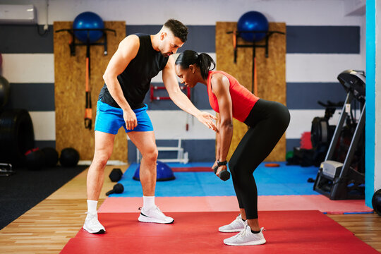 Personal trainer guiding a woman lifting weights during a workout session in a gym - Powered by Adobe