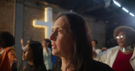 Close-up of women worshiping in group, expressing faith and unity, illuminated cross in the background symbolizing spirituality and devotion