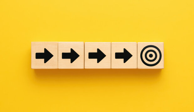 A sequence wooden blocks aligned on a yellow background illustrates focus and progression towards a central goal in business strategy