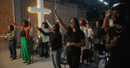 Congregation clapping hands in celebration during church service, illuminated cross and brick wall...