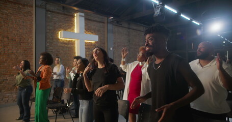 Diverse group of people clapping and smiling during worship in a church, glowing cross in...