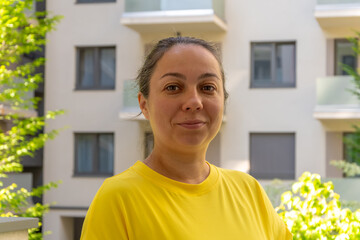 A 40-45 year old woman standing on the balcony or terrace of an apartment block.
