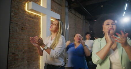 Diverse group of people clapping and smiling during worship in a church, glowing cross in...