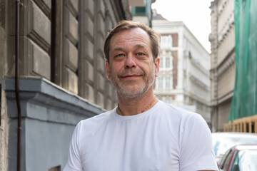Close-up of the face of a man of 50-55 years old with a beard and moustache, shot in the street. The expression of the face is calm and friendly.