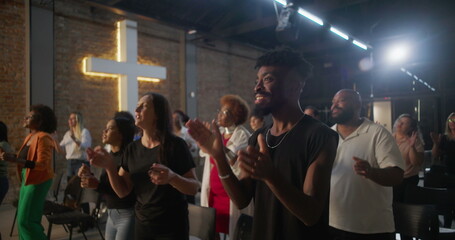 Multicultural congregation clapping and smiling during church worship, illuminated cross in background, expressions of faith, joy, unity, and spiritual devotion