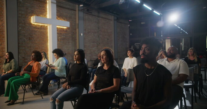 Congregation sitting during church service, listening attentively with illuminated cross in background, diverse community gathering for faith and spiritual connection