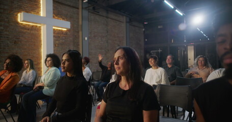 Obraz premium Woman sitting in church with thoughtful expression, illuminated cross and congregation in background, reflecting during worship service in sacred community gathering