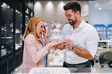 Happy couple enjoying a moment in a jewelry store, selecting a beautiful jewelry pieces together. Both are happy and smiling with love and excitement.