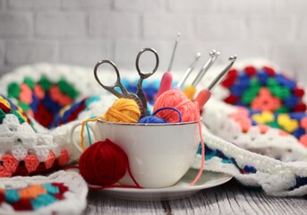 A cup and a saucer with clews balls of yarn wool and crocheted blanket handmade craft bright photo	