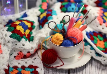 A cup and a saucer with clews balls of yarn wool and crocheted blanket handmade craft bright photo	