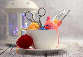 A cup and a saucer with clews balls of yarn wool and crocheted blanket handmade craft bright photo	