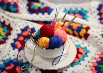 A cup and a saucer with clews balls of yarn wool and crocheted blanket handmade craft bright photo	