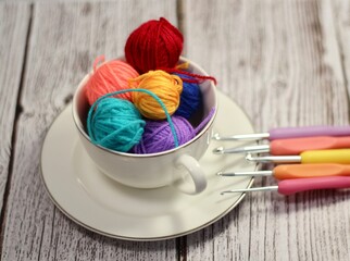 A cup and a saucer with clews balls of yarn wool and crocheted blanket handmade craft bright photo	