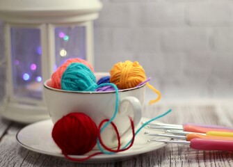 A cup and a saucer with clews balls of yarn wool and crocheted blanket handmade craft bright photo	