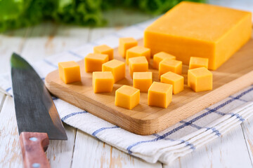 Cheddar cheese cut into cubes on light kitchen table, selective focus.