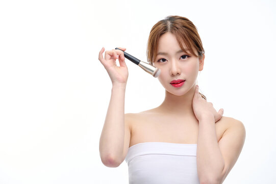 Young Woman Applying Makeup with Brush on White Background