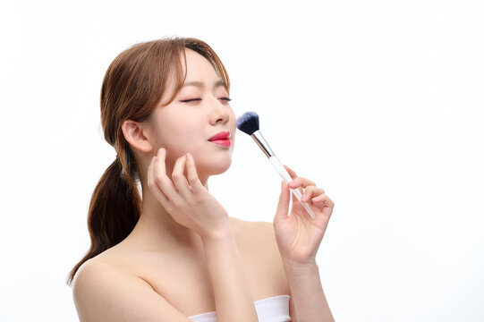 Young Woman Applying Makeup with Brush on White Background