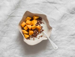 Delicious breakfast - Greek yogurt, crispy granola, fresh mango in a bowl on a light background,...