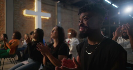 Congregation applauding during a heartfelt worship service, people engaged in faith and prayer, illuminated cross on a brick wall creating a spiritual atmosphere