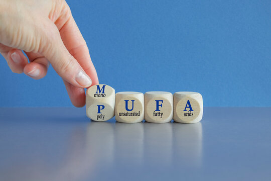 Hand turns a cube and form the acronym MUFA (Monounsaturated Fatty Acids) and PUFA (Polyunsaturated Fatty Acids). Beautiful blue background, grey table. Business and medical concept.