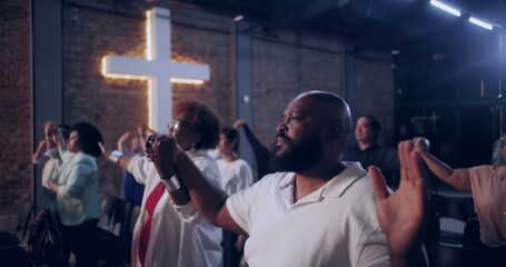 Congregation holding hands in unity, standing together during worship service, illuminated cross...