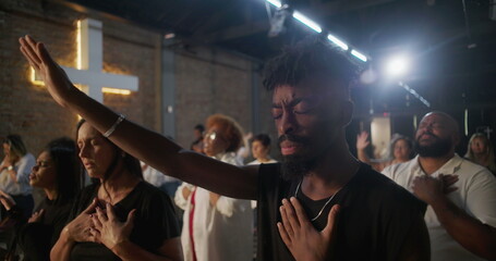 African American man in emotional worship, hand raised and over heart, glowing cross in background,...