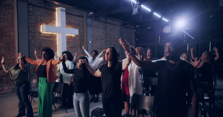 Congregation holding hands in unity, standing together during worship service, illuminated cross...