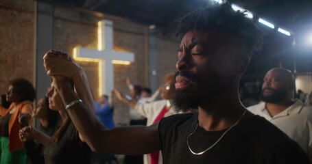 People holding hands during worship, expressing unity and faith, illuminated cross symbolizing spirituality and community in a heartfelt church service