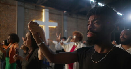 People holding hands during worship, expressing unity and faith, illuminated cross symbolizing...